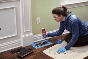 A woman uses expanding foam to fill air gap around vent